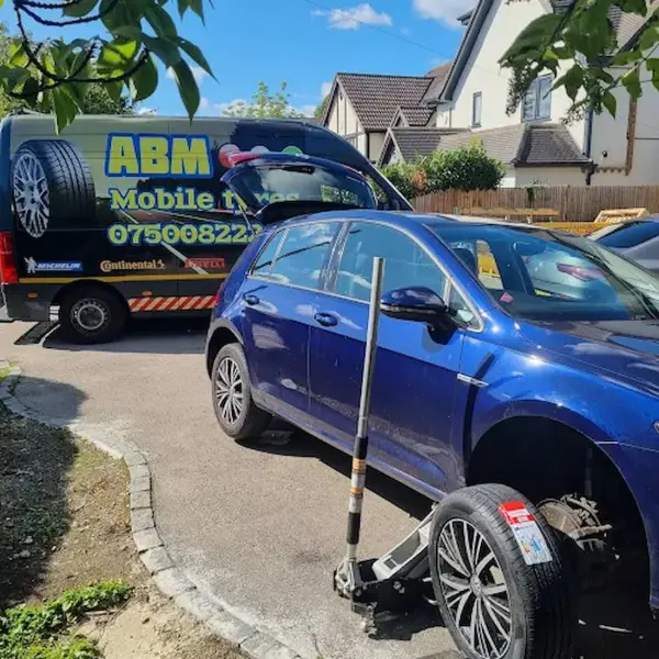 ABM Mobile Tyres van parked in a driveway replacing a tire on a blue VW Golf